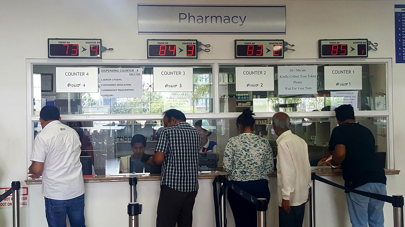 Hospital pharmacy with four dispensing counters, each with its own LED token and counter display above the window